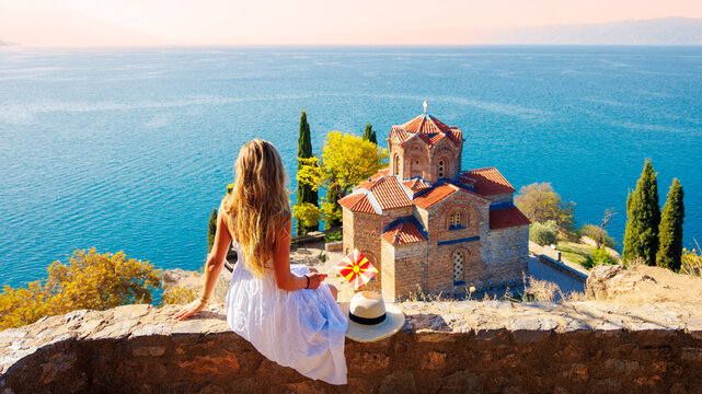 Young woman in white dress holding macedonian flag looking at Saint John Kaneo church, authentic travel experience at Ohrid lake in North Macedonia