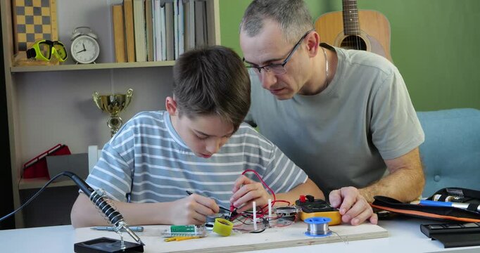 Boy tests electronic circuit with multimeter while father watches attentively and nods with approval. Vertical scene captures STEM learning, mentorship, practical skills and family bonding
