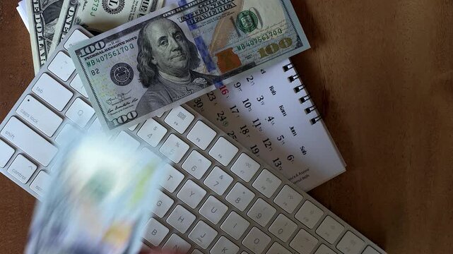Close up top down view of Asian male hand putting US dollar money bills on top of modern computer keyboard