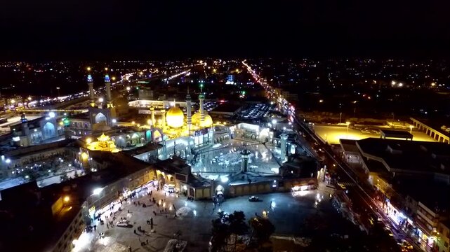 Incredible night aerial tracking shot revealing the interconnected main courtyards and majestic architecture of the holy shrine of Lady Masoumeh in Qom city, perfect for stock footage.