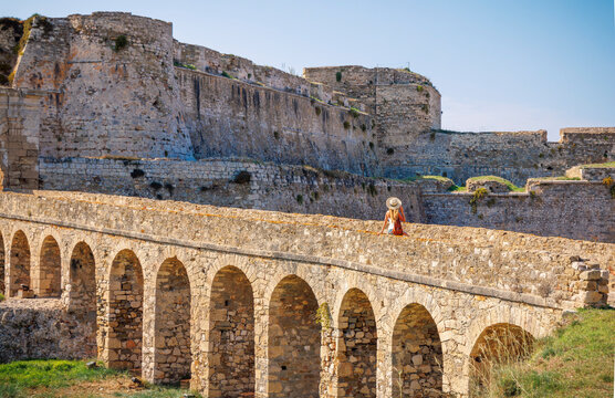 Young female tourist sitting on the ancient stone arch bridge leading to Methoni Venetian fortress, authentic historical exploration and travel adventure in Greece