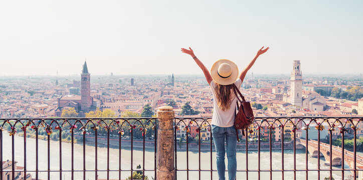 happy woman traveler arms raised looking at verona cityscape in italy