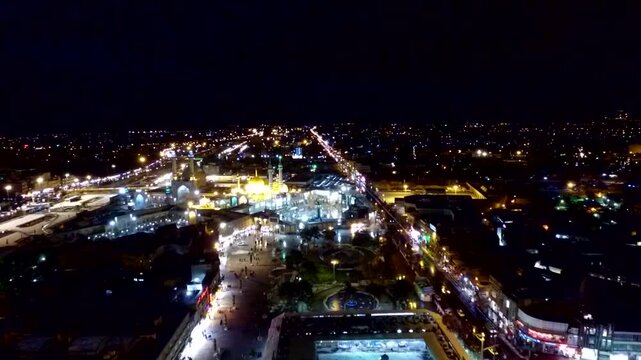 High-altitude aerial drone perspective panning over the illuminated holy shrine complex and sprawling urban city lights of Qom at night, capturing a spectacular landmarks travel film.