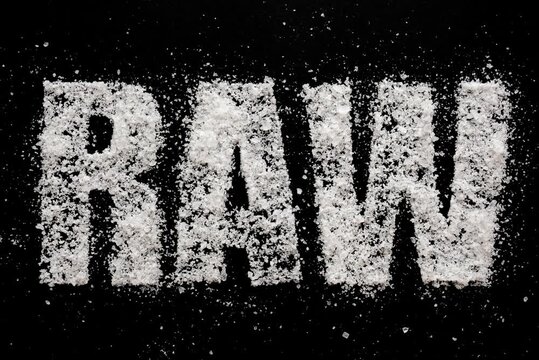Word raw written with white sea salt crystals on textured black background
