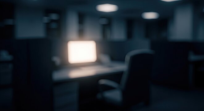 Glowing computer monitor illuminates a dark and empty office late at night.