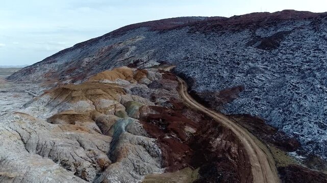 Beautiful drone tracking video moving alongside a remote hillside track carved into a massive salt dome ridge, highlighting the intricate geological strata and rugged alpine terrain scenery