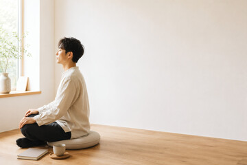 Obraz premium Asian Man Practicing Meditation at Home in Bright Minimal Interior with Copy Space