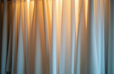 Obraz premium Close view of layered fabric swatches for curtains. Beige and light blue textiles hang in soft folds. Warm light glows from behind showing textile texture.