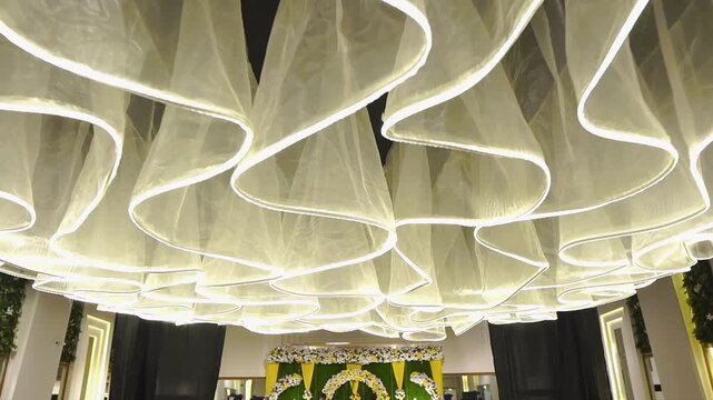 Luxury wedding hall interior featuring elegant flowing ceiling fabric installation, modern ambient lighting, and sophisticated decorative design. Ideal for wedding venues, banquet halls, event spaces,