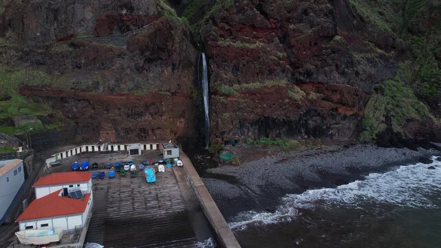 Majestic waterfall cascading down rugged cliffs into the Atlantic Ocean beside the charming fishing village of Paul do Mar, Madeira