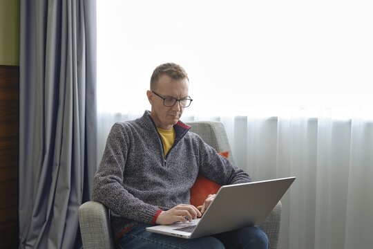 A middle-aged man sits comfortably in an armchair and watching as real estate agent showing a property through an online video call
