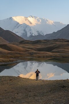 Hiker looking at mountain landscape, mountains reflected in a small mountain lake, Lenin Peak, Trans Alay Mountains, Pamir Mountains, Osh Province, Kyrgyzstan
