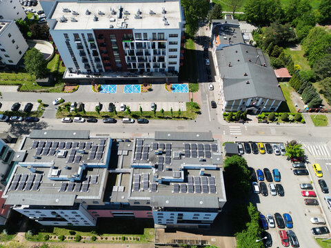 Aerial view of modern residential apartment buildings with solar panels on roofs and organized parking lot infrastructure.