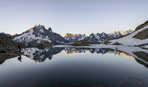 Tourist at a mountain lake in the morning, mountain landscape at sunrise, water reflection in Lac Blanc, mountain peak, Aiguille Verte, Grandes Jorasses, Aiguille du Moine, Mont Blanc, Mont Blanc massif, Chamonix-Mont-Blanc, Haute-Savoie, France