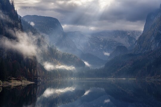 The Vordere Gosausee in autumn. The Dachstein in clouds. Rays of sunshine shine through the clouds. Forest shrouded in clouds. Vorderer Gosausee, Gosau, Gosau Valley, Salzkammergut, Upper Austria, Austria