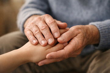 Fototapeta premium Close-up of elderly hands gently holding a younger person’s hand, symbolizing care, support, compassion and intergenerational connection.