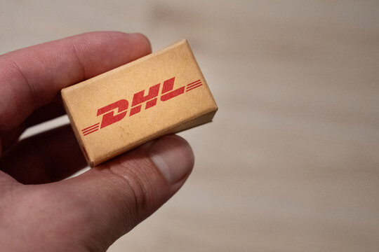Warsaw, Poland - Jan 11, 2026: Close-up of hand holding a small DHL package, symbolizing logistics and express delivery services in an urban setting.