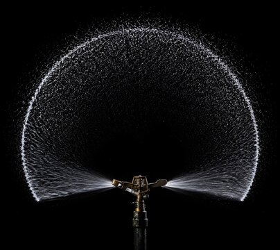 High Speed Photo of Rotating Lawn Sprinkler Head Creating Perfect Half Circle Water Arc Background