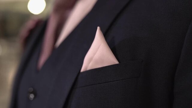 Close-up detail shot of a pink decorative ribbon attached to the groom's suit during a wedding celebration. Elegant wedding fashion accessory captured with selective focus and soft background blur, hi