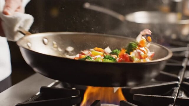 A chef seasons fresh vegetables cooking in a hot metal pan on a stove