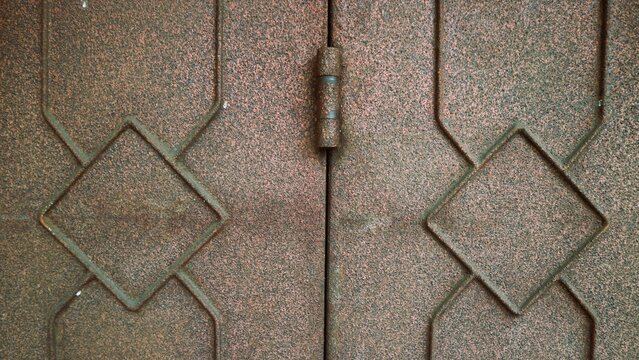 Close-up of a vintage metal door with diamond-shaped patterns and a central hinge