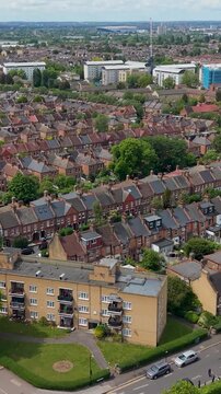 Drone flight Walthamstow to Tottenham over Victorian terraced houses, forest road and Lloyd Park on right, with Tottenham Hotspur Stadium visible on horizon, London, UK. Vertical format.