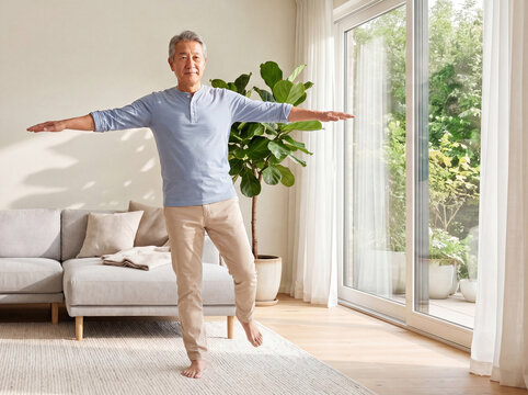 Healthy senior Asian man practicing a standing balance exercise at home, improving stability, mobility, and confidence as part of an active aging lifestyle.