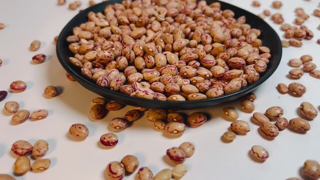 Camera Rotating Around Black Plate of Raw Pinto Beans Close-up, Dried Organic Cranberry Beans Orbit Panning Right to Left, 16:9 Landscape Pulses Stock Footage