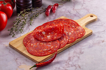 Naklejka premium Spicy salami slices on wooden cutting board with fresh tomatoes and chili peppers