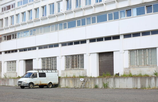 A lonely old rusty white minibus is parked near a white industrial building, Badayeva Street, Saint Petersburg, Russia, June 12, 2026