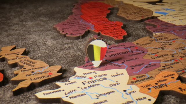 A close up view of a wooden map of europe with a belgium flag pin highlighting its location.