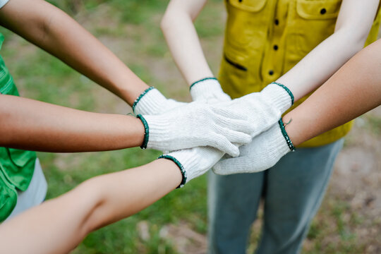 People wearing working gloves stacking hands together, showing strong teamwork, unity, and collaboration during a community volunteering event outdoors