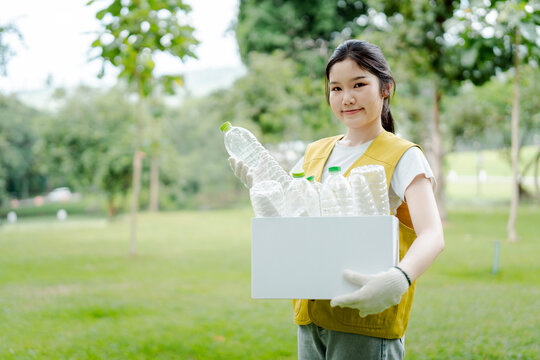 Asian woman volunteer in protective gloves collecting plastic bottles from garbage in a park, contributing to environmental protection and sustainability efforts