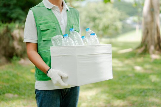 Person carrying a container of plastic bottles, demonstrating commitment to waste management, recycling, and sustainability in an outdoor park setting