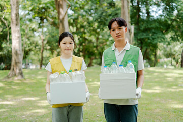 Fototapeta premium Young asian volunteers collect and sort plastic bottles in a green park cleanup, promoting recycling, teamwork and sustainable community action for a healthier environment
