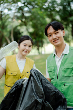 Young volunteers collecting plastic litter in garbage bags, actively working to clean up a park for environmental conservation, sustainability, and ecology awareness