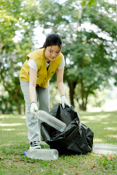 Young asian woman volunteering for environmental protection, collecting plastic bottles in a public park, focusing on recycling and sustainable living initiatives