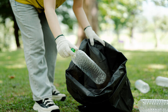 Person wearing gloves picking up plastic bottle from grass, placing it into a black garbage bag, symbolizing environmental clean-up, conservation, and volunteer work