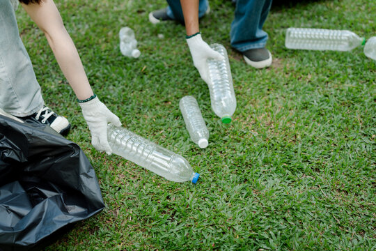 People in protective gloves volunteering together, collecting discarded plastic bottles and litter from green grass, promoting cleanup and sustainability