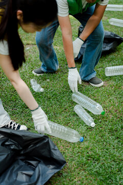Volunteers collecting plastic bottles from green grass, placing them into a black trash bag while participating in an environmental cleaning and recycling initiative