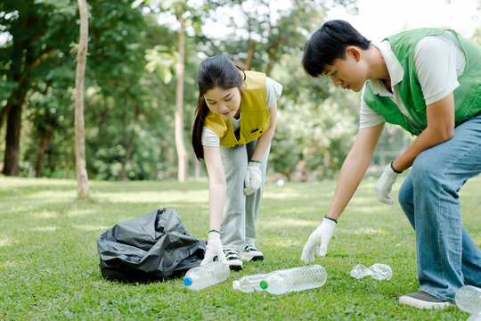 Young environmental volunteers collecting plastic bottles and litter from green park grass, promoting sustainability and community cleanup for a healthier nature