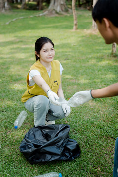 Young asian female volunteer working with team members, collecting plastic bottles in a public park, contributing to environmental protection and community recycling initiative