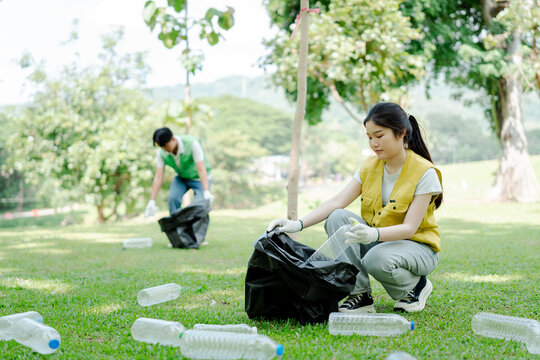 Young asian volunteers are clearing plastic bottle waste from a park's green grass, actively working towards environmental conservation and recycling for a cleaner future