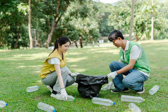 Two young volunteers pick up plastic bottles from a green lawn into a black trash bag during a park cleanup, promoting recycling, sustainability and community environmental action