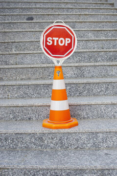 Orange and white road cone with red stop sign on stairs