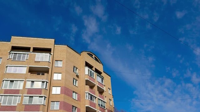 Brick apartment building against blue sky, sunlit multi storey facade with balconies and windows, textured masonry and corner