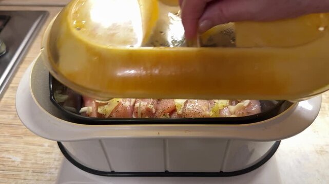 Close-up steamed chicken fillet in steamer, woman opens lid to check garlic seasoning on fresh poultry inside electric double