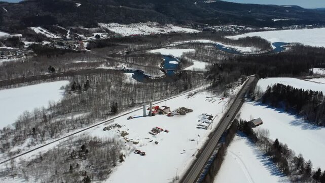 Panoramic drone footage of the Matapedia River winding through snowy forests, crossed by a bridge linking Route 132 beneath the Appalachian Mountains.