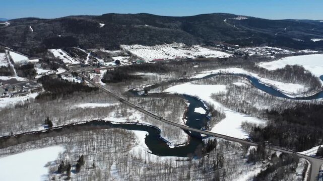 Panoramic drone footage of the Matapedia River winding through snowy forests and farmland beneath the Appalachian Mountains in Quebec, Canada.