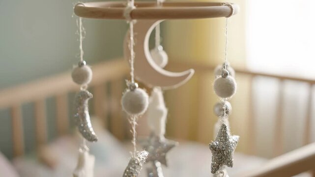 Baby mobile featuring silver stars and moons hanging above a crib, showcasing a gentle rotation in a softly lit nursery environment with pastel colors